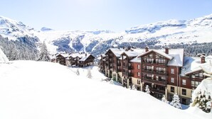 Una località montana innevata con edifici in stile chalet, una pista da sci e un cielo sereno.