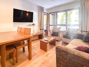 A living room with a wooden table, chairs, a sofa, and a TV mounted on the wall.
