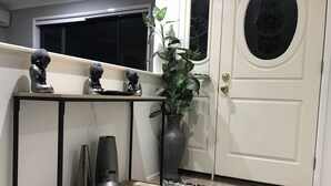 Un corridoio con una porta bianca, un tavolino con oggetti decorativi, una pianta in vaso e un tappeto decorato.