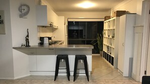 Una cucina compatta con un'isola centrale, due sgabelli, una sveglia e un frigorifero.