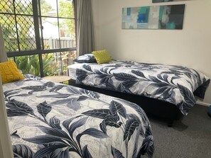 A room with two beds, each with a floral-patterned bedspread. There is a window with a view of greenery outside.