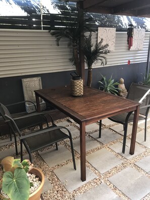 A patio area with a wooden table and chairs, surrounded by potted plants and a Buddha statue.