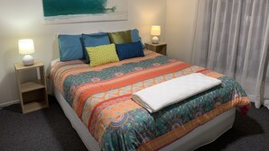 Un letto rifatto con una coperta colorata e un motivo decorativo, due lampade ai lati del letto e un grande quadro raffigurante un'onda marina sopra il letto.
