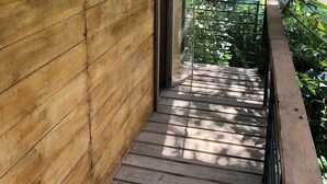 Pared exterior de madera con barandal metálico y puerta que da a un espacio al aire libre cubierto.