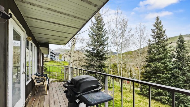 A wooden deck with a grill, chairs, and a view of trees and hills.