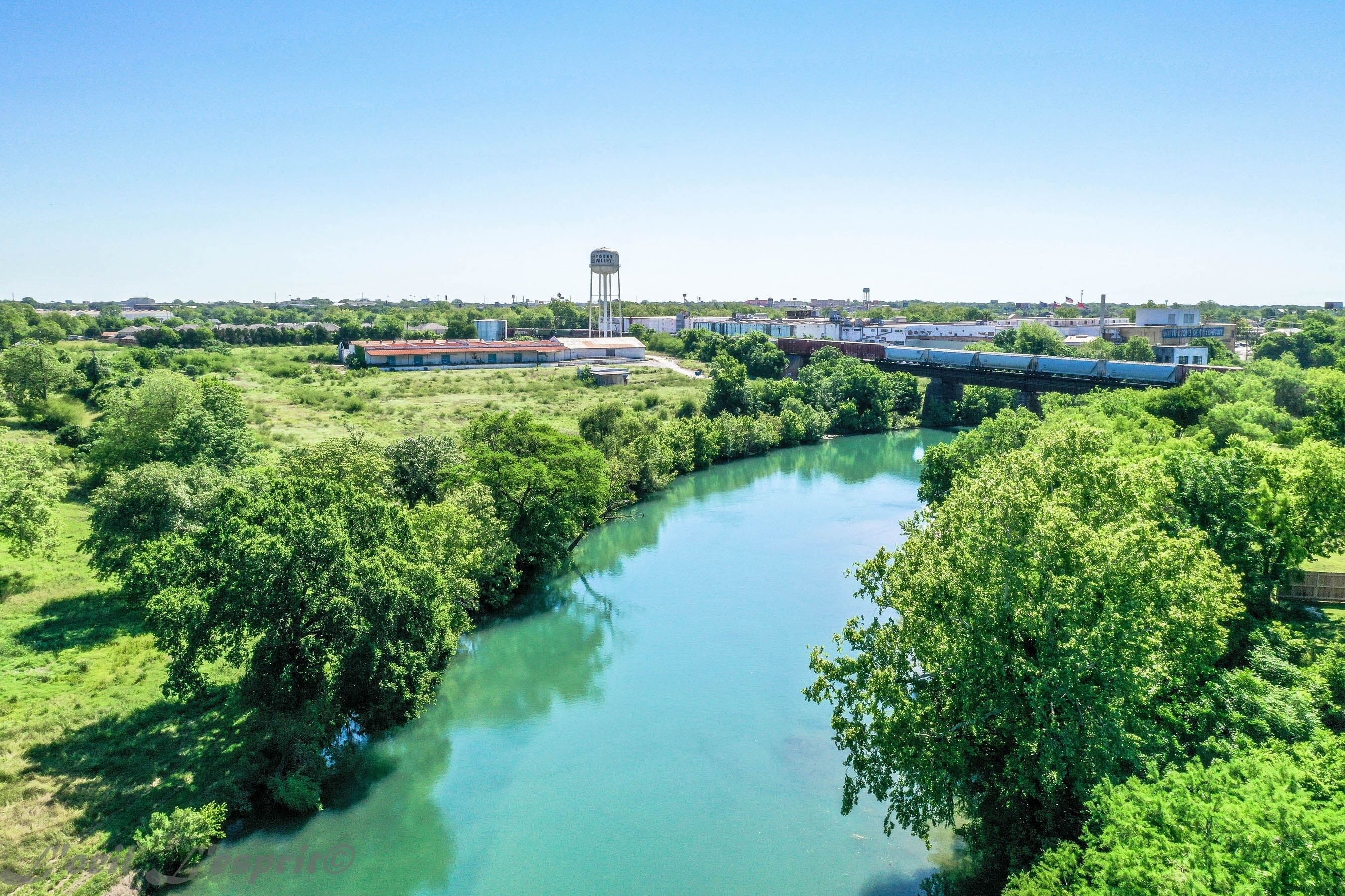 A river with a bridge, surrounded by greenery and buildings.