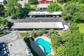 An aerial view of a hotel with a swimming pool, parking lot, and adjacent buildings.