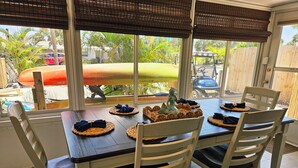 A dining area with a table set for four, surrounded by chairs, with a view of a pool and palm trees outside. - Heated Pool, Bikes, Kayaks, Sups, Outdoor Tiki Bar with TV! & Corn Hole Court (Englewood)