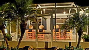 A conservatory with glass walls, wooden furniture, and palm trees. - Heated Pool, Bikes, Kayaks, Sups, Outdoor Tiki Bar with TV! & Corn Hole Court (Englewood)