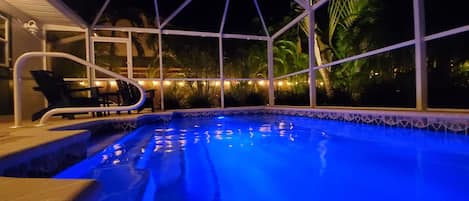 An indoor swimming pool with a geometric glass enclosure, surrounded by chairs and palm trees.