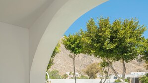 A white-walled outdoor seating area with a stone-tiled floor, a small table, and a potted plant. - Luxury Three Bedroom apartment with hot tub "L&E" (Santorini)