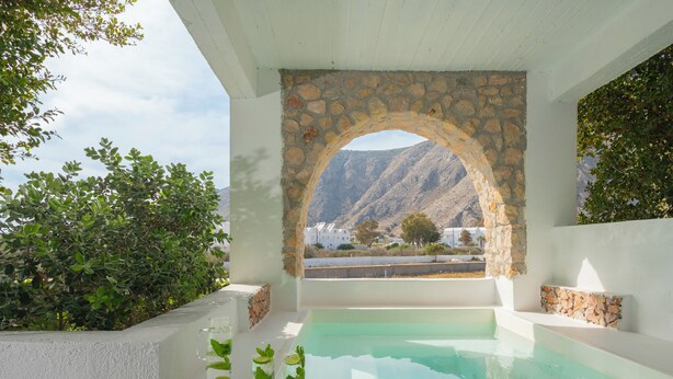 A pool area with a stone archway, surrounded by greenery and a mountainous backdrop. - Luxury Three Bedroom apartment with hot tub "L&E" (Santorini)