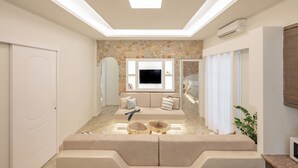 A modern living room with a built-in TV, a stone accent wall, and a cozy seating area. - Luxury Three Bedroom apartment with hot tub "L&E" (Santorini)