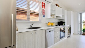 A modern kitchen with white cabinetry, a stainless steel sink, and a yellow kettle. There is a fire blanket sign on the wall and a window with blinds. - Arklow - Pet Friendly with Ocean Views (Culburra Beach)