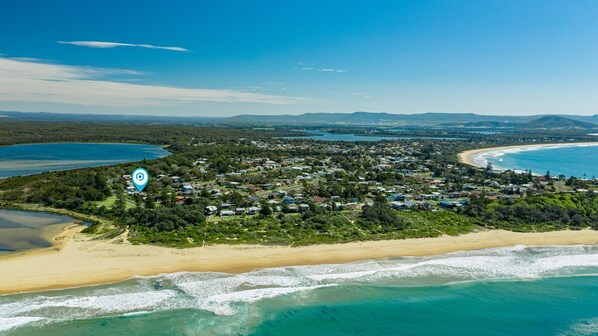 An aerial view of a coastal town with beachfront properties, dense greenery, and a clear blue sky. - Arklow - Pet Friendly with Ocean Views (Culburra Beach)