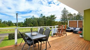 Una terraza de madera con una mesa y sillas, un sofá y una barandilla con vistas a un paisaje verde.