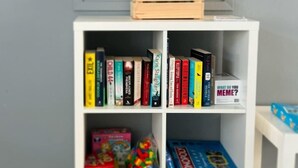 Een witte boekenkast met boeken en een Monopoly speldoos.