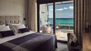 Une chambre d’hôtel moderne dotée d’un grand lit, d’un balcon avec vue sur l’océan et d’une porte-fenêtre coulissante.