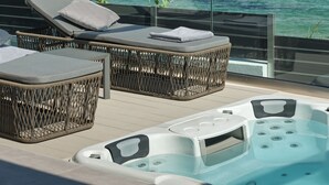 Un balcon doté de meubles en osier et d’un jacuzzi, offrant une vue imprenable sur une mer d’un bleu profond.