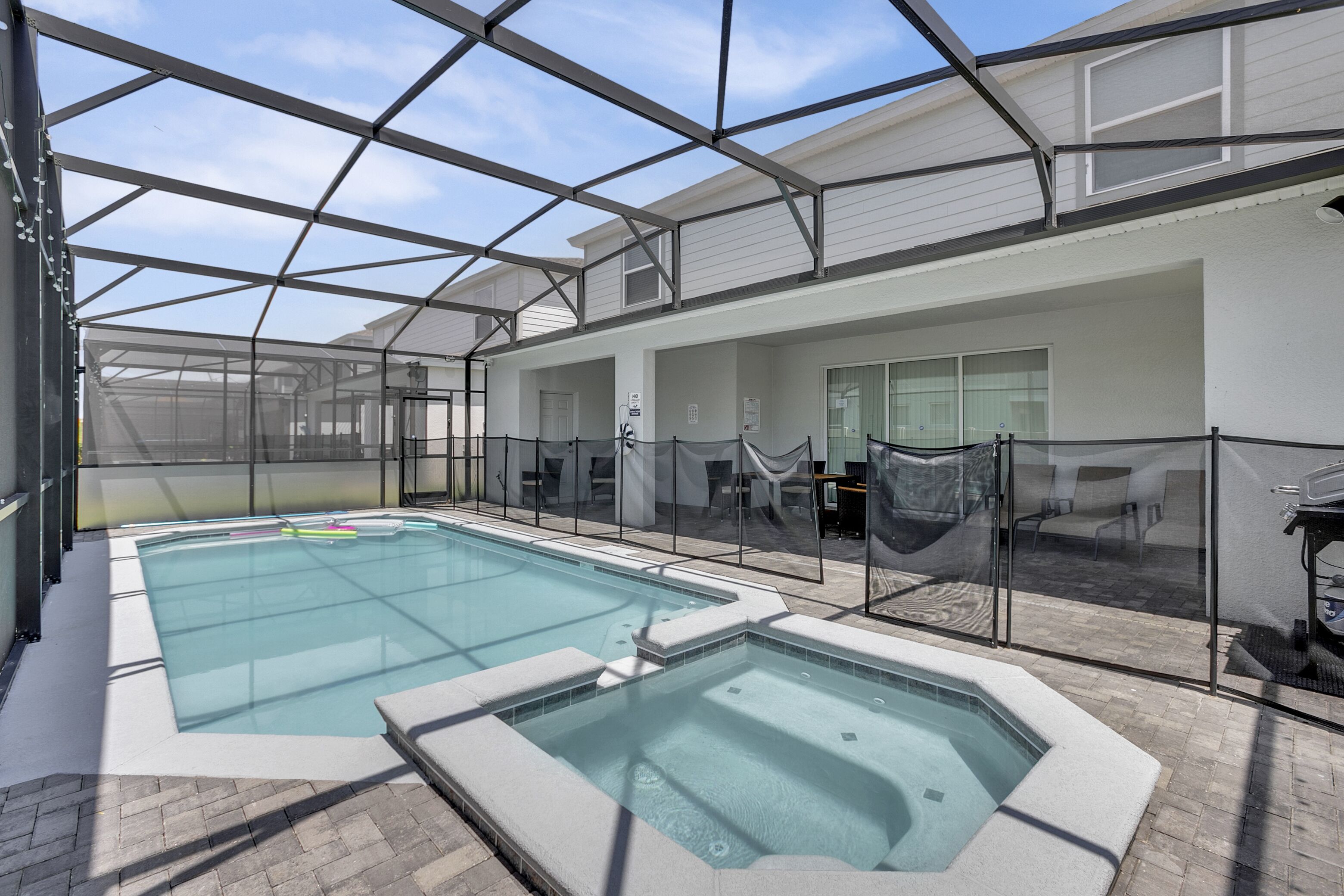 Uma área de piscina coberta com paredes de vidro e um espaço de varanda com mobiliário para exterior.