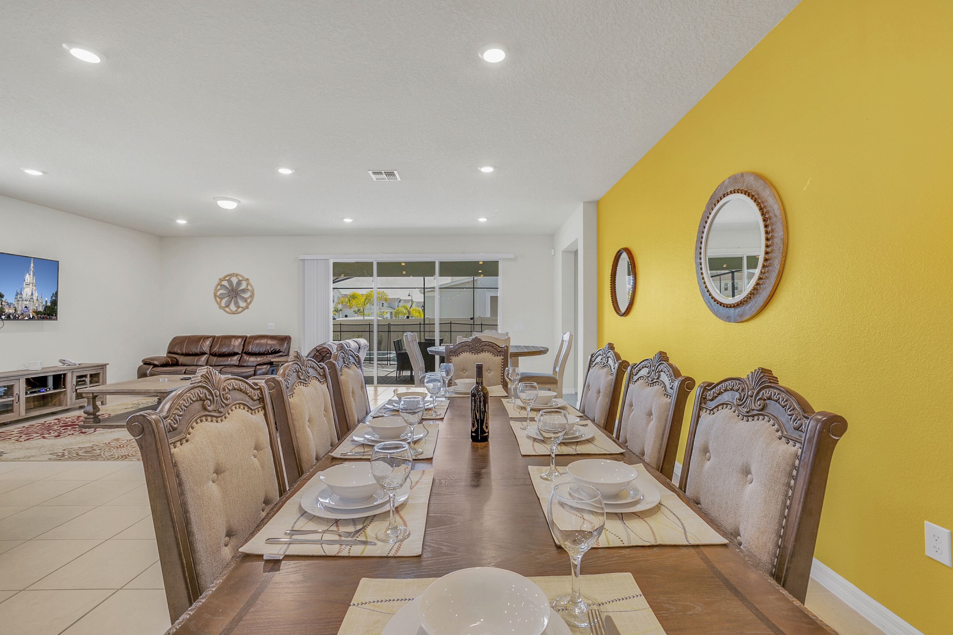 A dining room with a long wooden table set for six, surrounded by upholstered chairs with tufted backs.