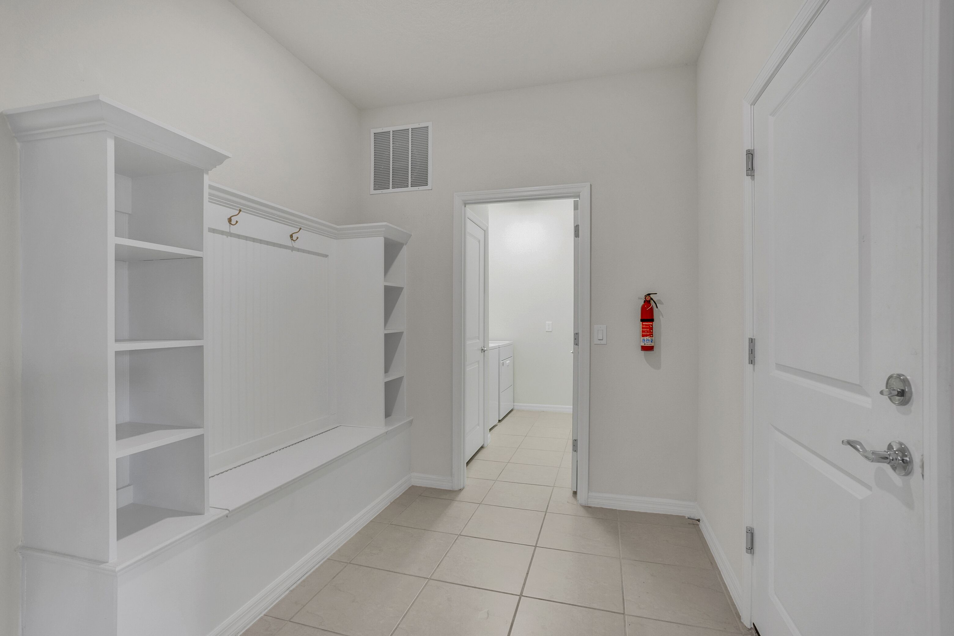 A hallway with a built-in closet, a fire extinguisher, and a door leading to another room.