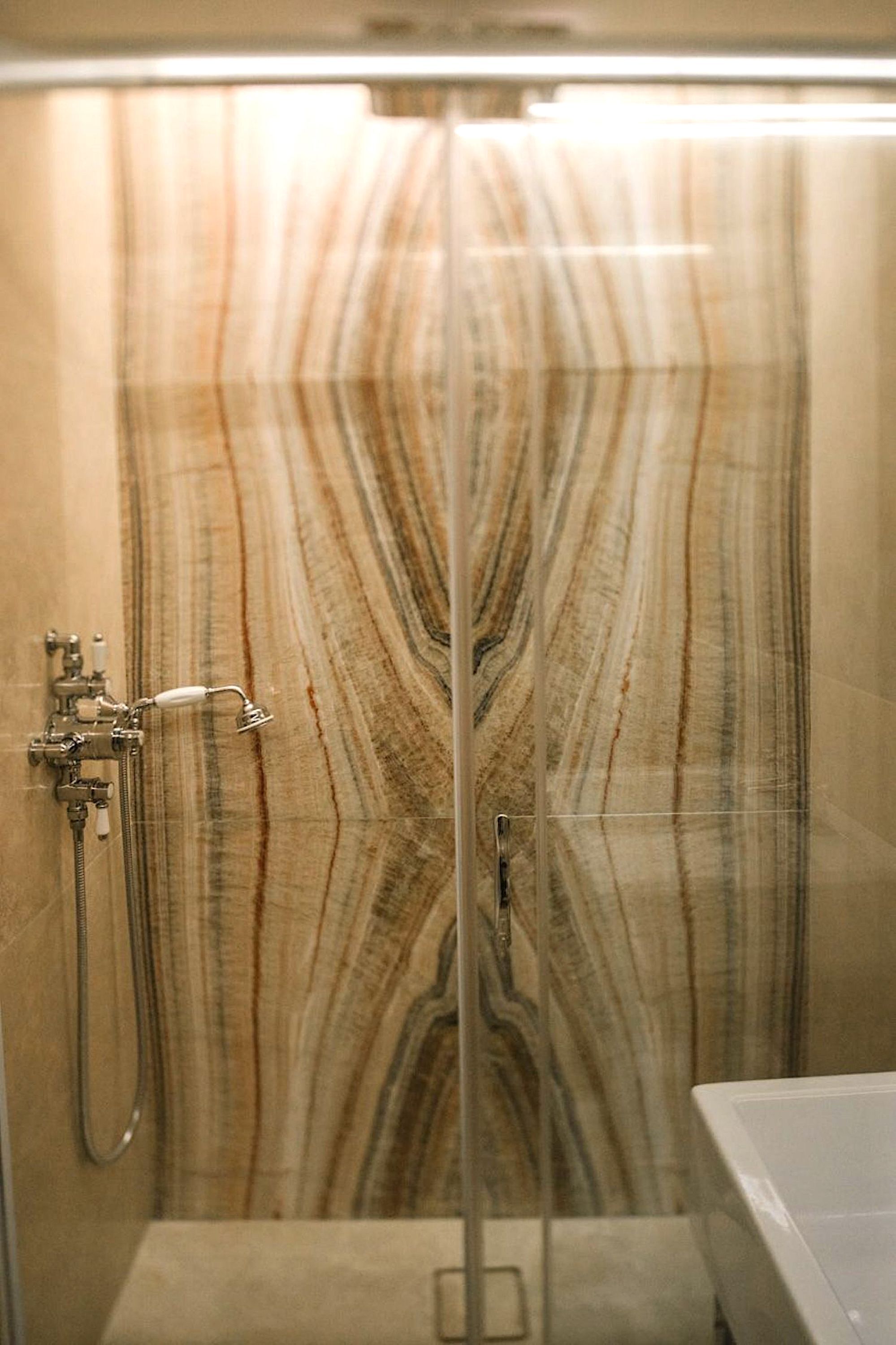 A bathroom with a marble shower wall and a modern showerhead.