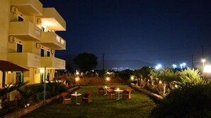 A hotel with outdoor seating and a well-lit garden area at night. - Cretan Family (Hersonissos)