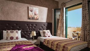 A hotel room with two beds, a large window with curtains, a painting on the wall, and a view of the outside. - Cretan Family (Hersonissos)