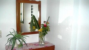 A wooden dresser with a mirror above it, a potted plant, and a vase with flowers. - Cretan Family (Hersonissos)