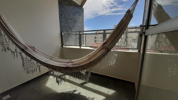 A hammock on a balcony with a view of buildings and a clear sky.