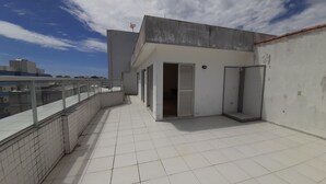 A rooftop terrace with a tiled floor, a concrete wall, and a metal railing.