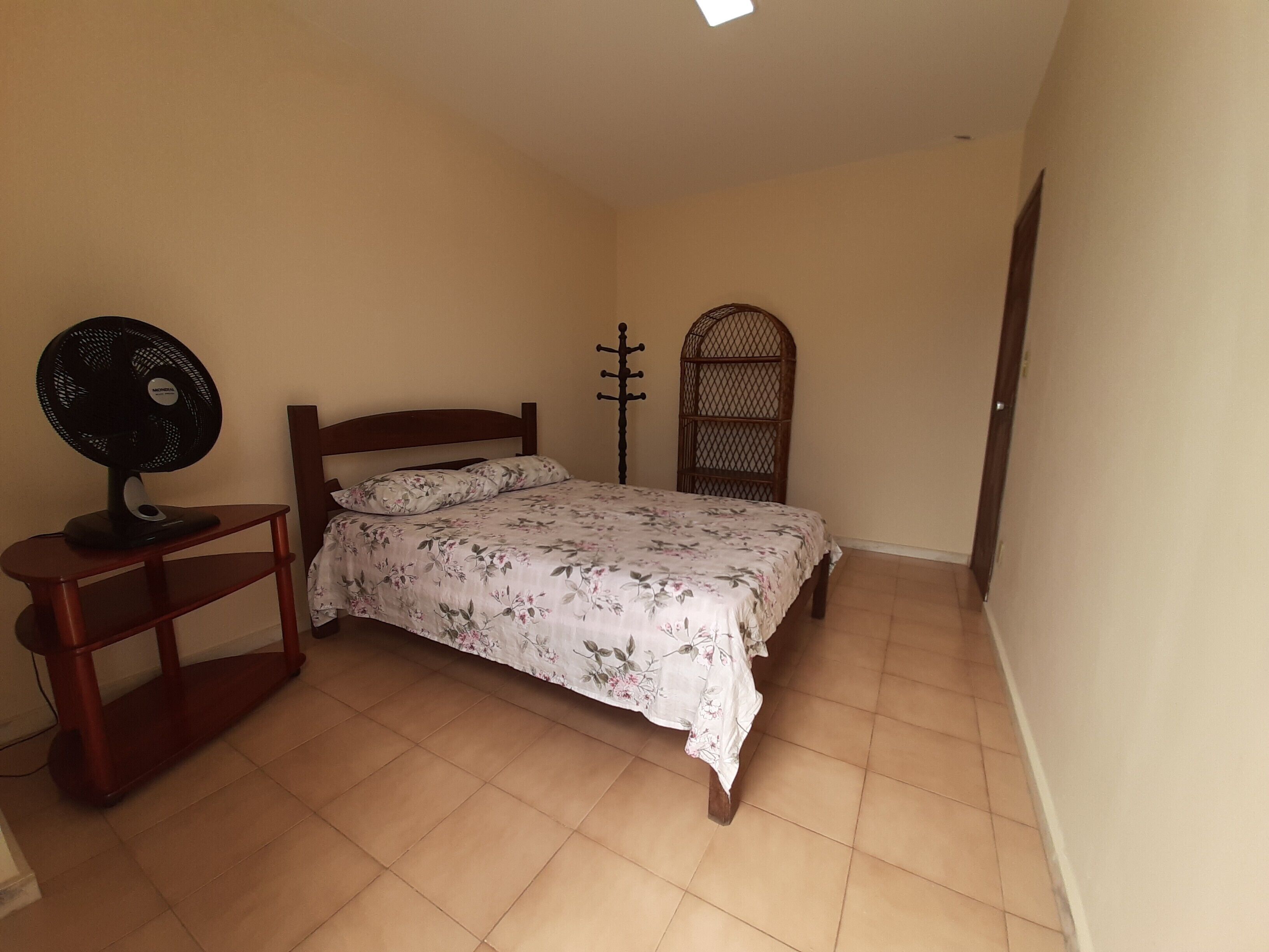 Een slaapkamer met een bed, een ventilator en een decoratief houten object.