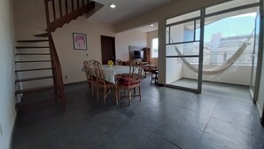 A spacious living area with a dining table, chairs, a staircase, and a large sliding glass door leading to a balcony.