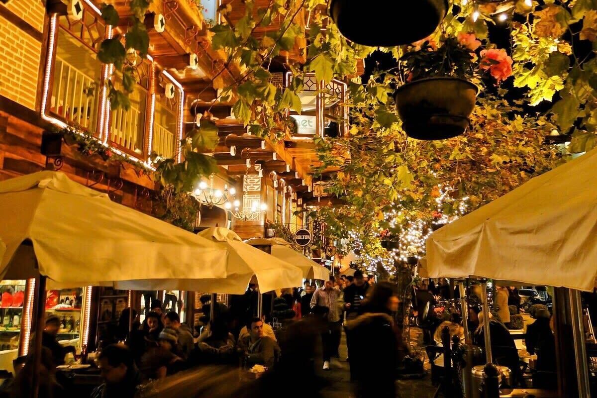 Una calle animada con mesas al aire libre y faroles colgantes.