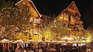 Un edificio con varias salas de comedor, mesas al aire libre y un gran árbol en la fachada.