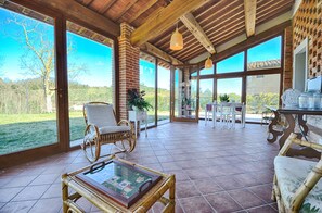 Un patio amplio con mobiliario de mimbre, ventanas grandes y vistas al exterior.