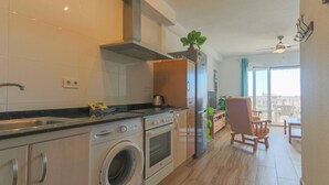 Eine moderne Küche mit Edelstahlgeräten, einem Einbauofen und einer Waschmaschine. Es gibt einen Essbereich mit Tisch und Stühlen, und durch große Fenster hat man einen Blick auf die Stadt.