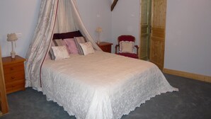 A bedroom with a four-poster bed, a wooden ceiling beam, a chair, and a nightstand with a lamp. - Luxury gite for adult couples, peaceful, open views, large swimming pool (Boisse)