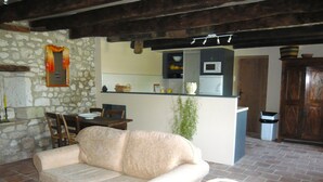 A cozy living room with a sofa, a dining table, and chairs. A kitchen area with a microwave and a sink is visible in the background. - Luxury gite for adult couples, peaceful, open views, large swimming pool (Boisse)
