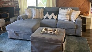 A living room with a grey sectional sofa, patterned cushions, a wooden coffee table, and a brick fireplace. - Cozy Condo in a great location! (Mammoth Lakes)