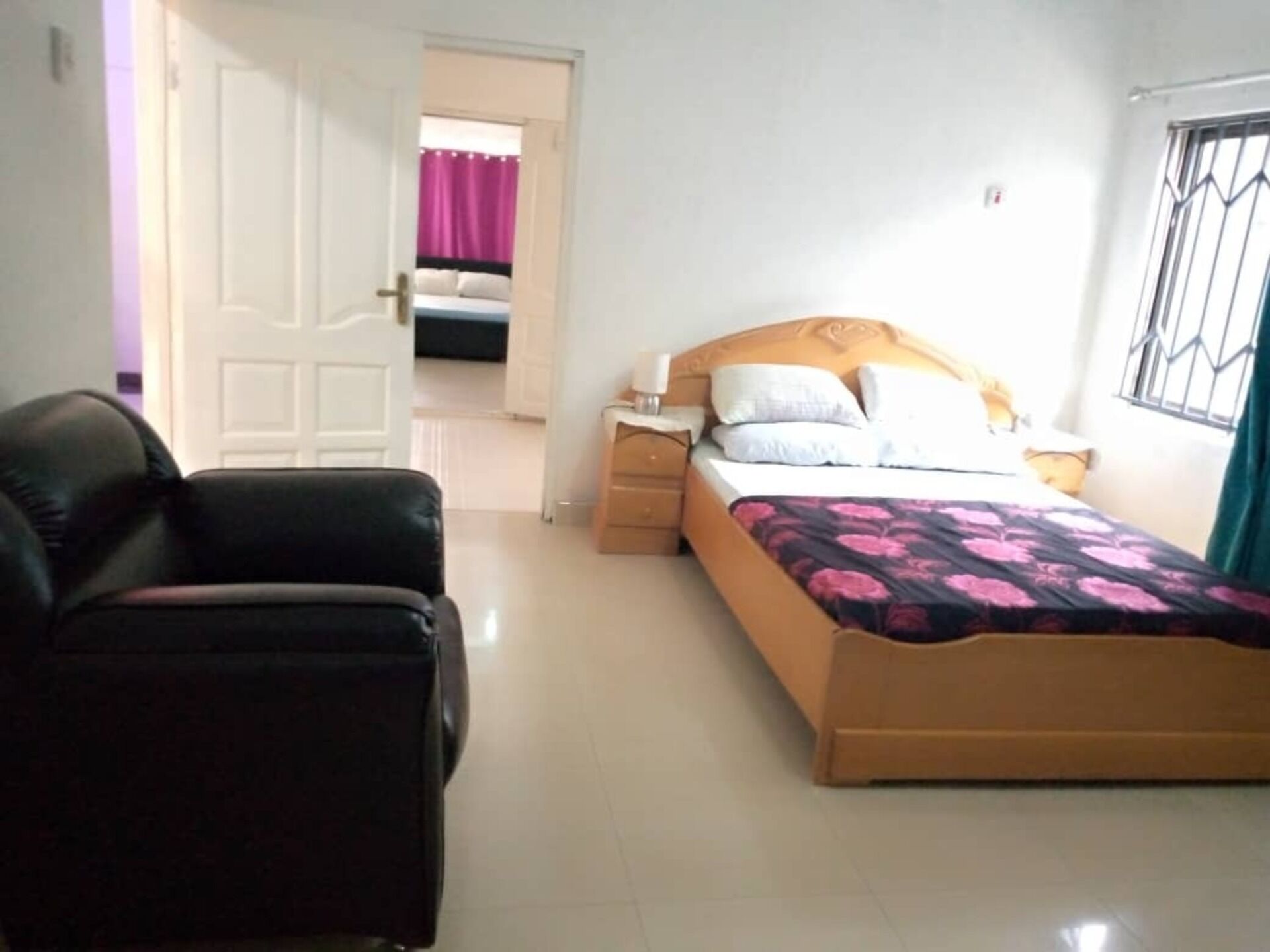A bedroom with a bed, a nightstand, a chair, and a door leading to another room.