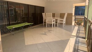 A room with a green folding table, white chairs, a tiled floor, and a balcony with a railing. - Kumasi Atonsu Dompoase Cozy Apartment (Kumasi)