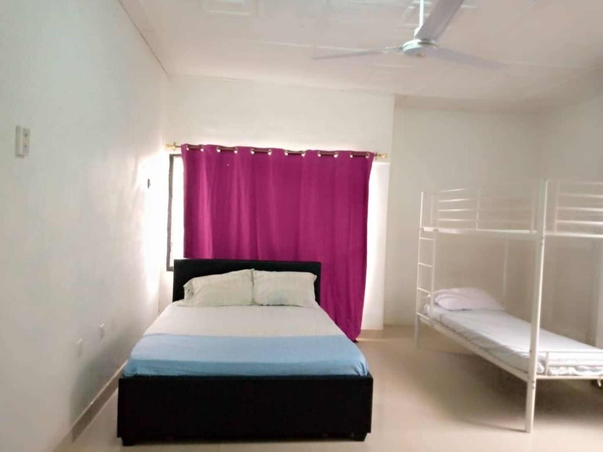 A bedroom with a single bed, a bunk bed, a ceiling fan, and a window with purple curtains.