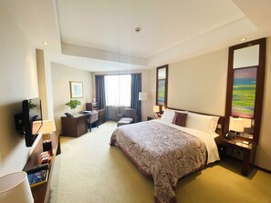 Een hotelkamer met een bed, bureau, stoel, televisie en een schilderij aan de muur.