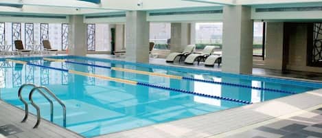 An indoor swimming pool with clear lanes, sunroof, and lounge chairs along the side.