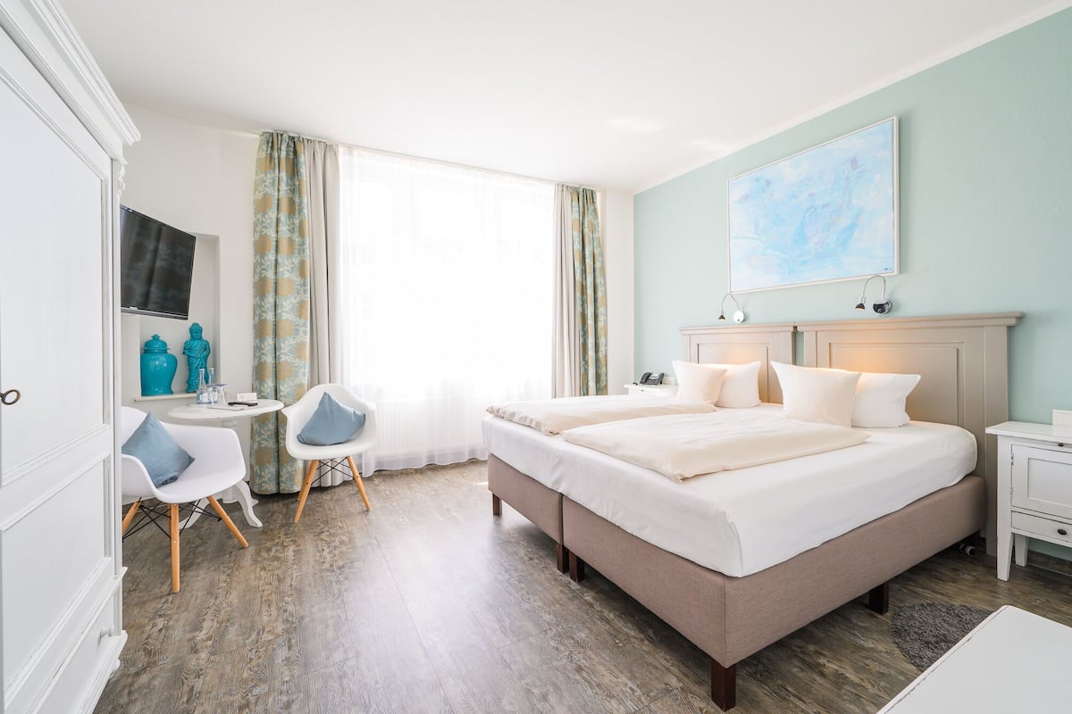 Une chambre d’hôtel avec un grand lit, deux tables de chevet, un bureau avec une chaise, une fenêtre avec des rideaux et un tableau au mur.