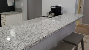 A kitchen with a granite countertop, a coffee machine, and a fish-shaped decoration on the wall. - Great Island Getaway! (Holmes Beach)