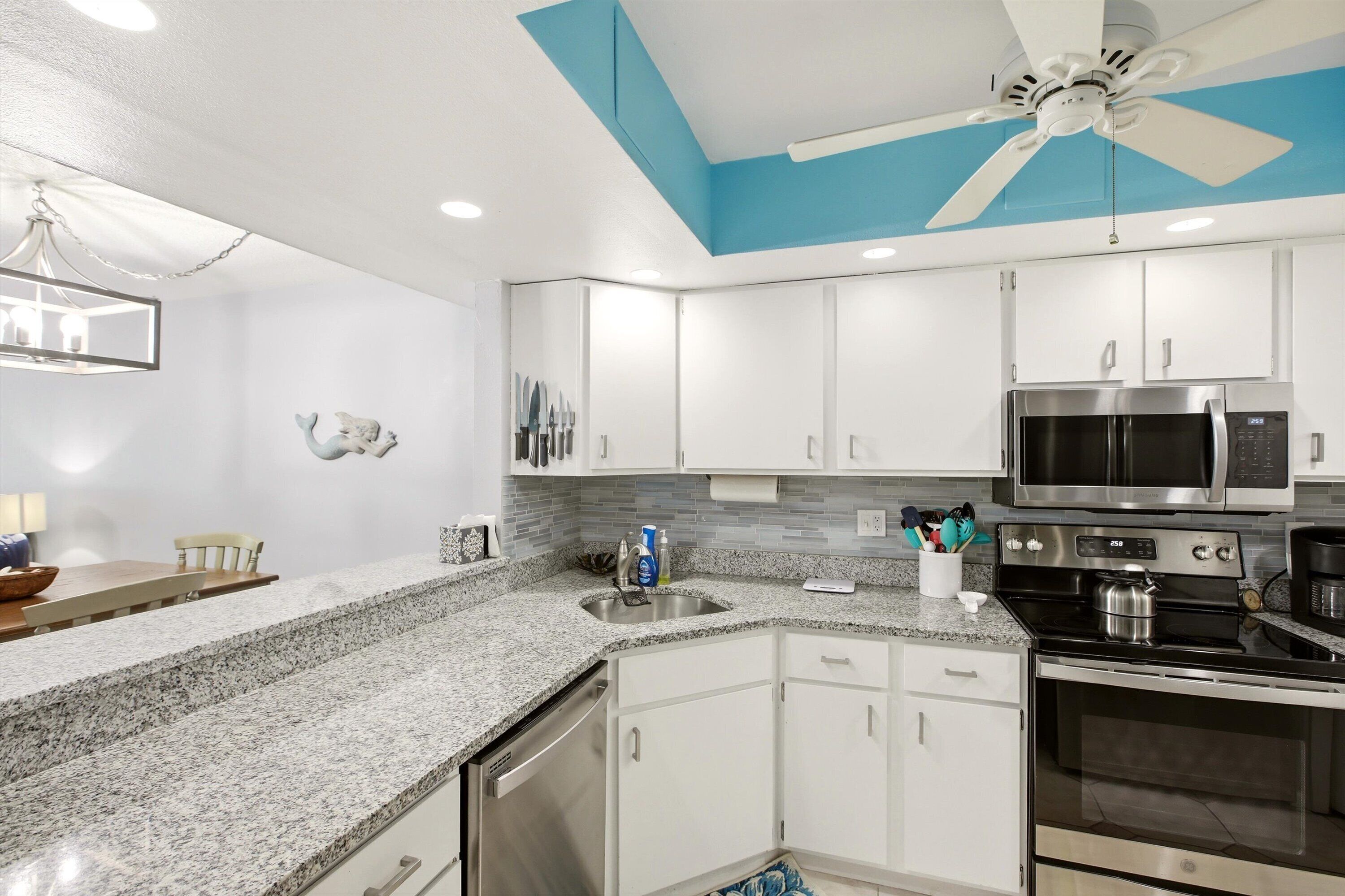 A kitchen with white cabinets, a granite countertop, a microwave, an oven, and a ceiling fan.