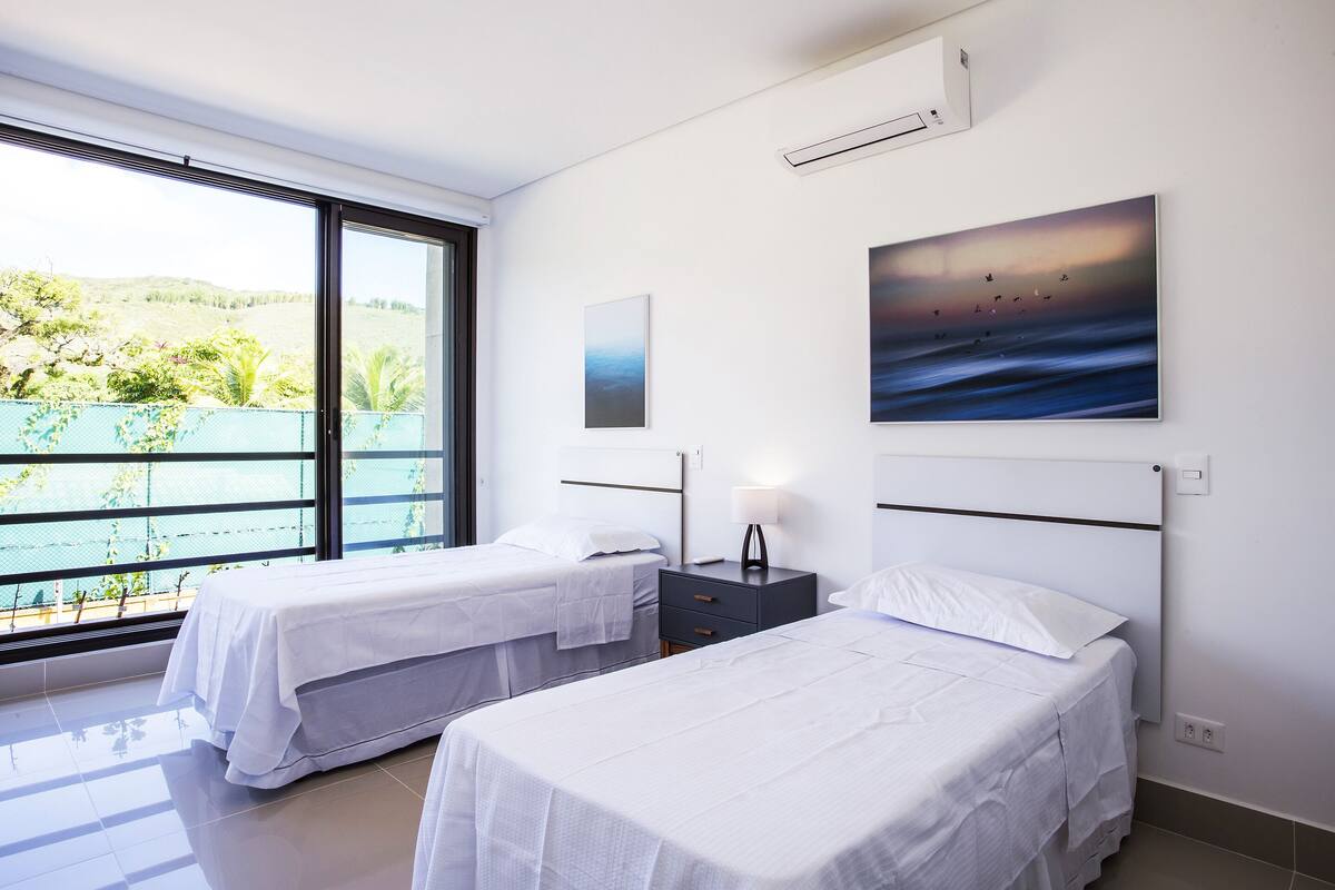 Une chambre d’hôtel avec deux lits, une grande fenêtre donnant sur un paysage verdoyant et une étendue d’eau, et un tableau accroché au mur.